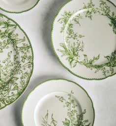 four plates with green floral designs on them sitting on a white tableclothed surface