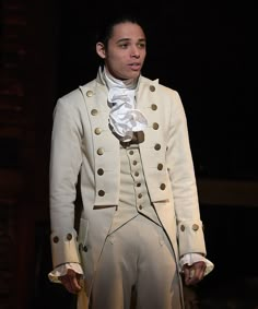 a man dressed in white is standing on stage with his hands in his pockets and looking to the side