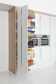 an open cabinet in the middle of a kitchen with food items on shelves next to it