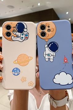 two people are holding up cell phones with cartoon images on the back and one is wearing an astronaut's helmet