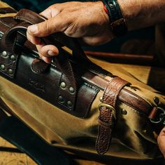 a person holding a brown and tan bag on top of a wooden table with other items in it