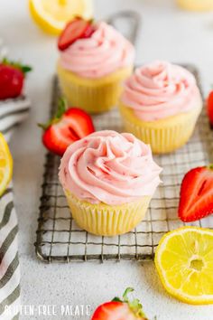 cupcakes with pink frosting and strawberries on a cooling rack next to lemon slices