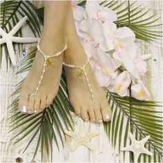 a woman's feet with pearls and starfish on the beach next to flowers