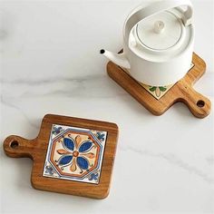 two wooden coasters and a teapot on a marble counter top with white background