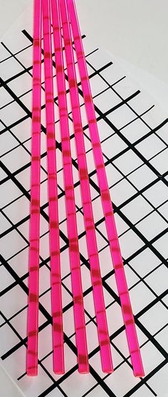 four pink sticks sitting on top of a black and white grid pattern with one red stick sticking out of it's center