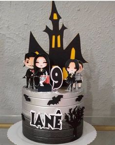 a halloween themed cake with spooky figures and decorations on the top, in front of a white wall