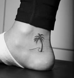 a small palm tree tattoo on the side of a woman's foot, which has a wave coming out of it