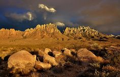 the mountains are covered in large rocks under a dark sky with fluffy clouds above them