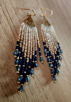 a pair of blue and white beaded earrings sitting on top of a wooden table