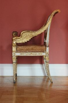 an antique chair with wings on it in front of a red wall and hardwood floor