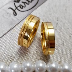 two gold wedding rings with white pearls on the bottom and one yellow ring in the middle