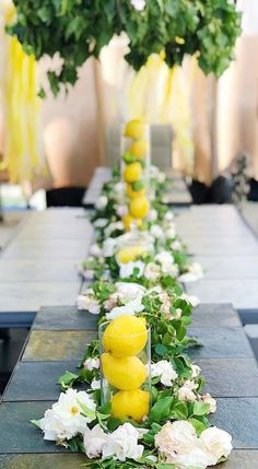 a long table with lemons and white flowers on the side, surrounded by greenery