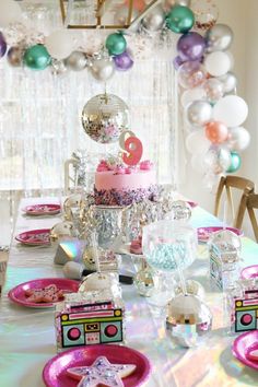 a table topped with plates and cake next to balloons