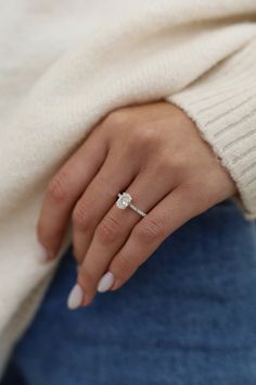 a woman's hand with a diamond ring on her left wrist, wearing blue jeans and a white sweater