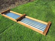 a wooden bench sitting in the middle of some green grass with metal tubes attached to it