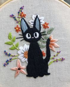 a black cat with flowers on it's back is sitting in front of a hoop