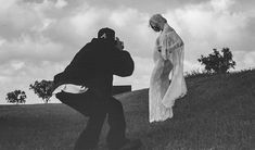 a man taking a photo of a woman in a wedding dress on a hill side