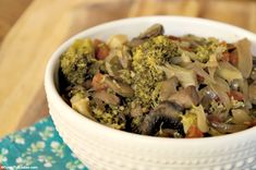 a white bowl filled with broccoli and mushrooms on top of a wooden table