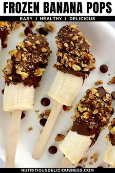 three frozen banana pops on a white plate with chocolate chips and chopped walnuts in the middle