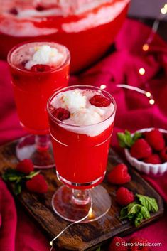 two glasses filled with ice cream and raspberries on a wooden tray next to a bowl of strawberries