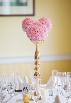 a heart shaped rose centerpiece on top of a table with wine glasses and place settings