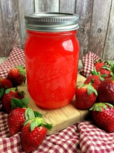 a jar filled with red liquid sitting on top of a cutting board next to strawberries