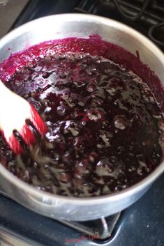 blueberry sauce being stirred in a silver pot on the stove with a red spatula