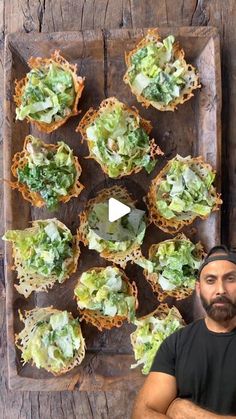 a man standing in front of a wooden tray filled with cupcakes covered in lettuce