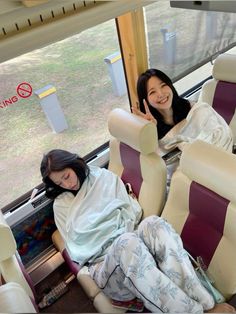 two women sitting on seats in front of a window with one holding up the peace sign