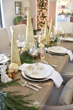 the table is set for christmas dinner with silverware and gold decorations on top of it