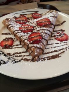 a white plate topped with chocolate covered pastries and sliced strawberries on top of it