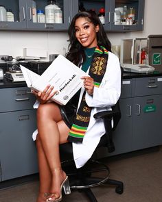 a woman sitting on a chair in a lab holding a piece of paper and smiling at the camera