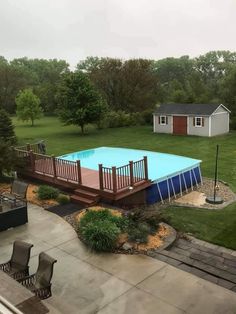 an above ground swimming pool surrounded by grass and wooden decking with chairs around it