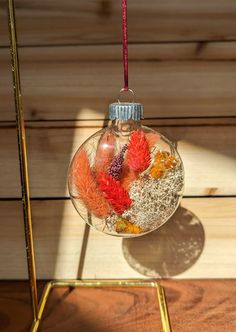 a glass ornament filled with dried flowers and leaves hanging from a red cord