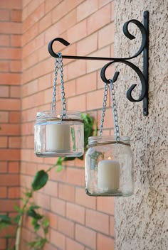 two glass jars hanging from a hook on a brick wall next to a candle holder