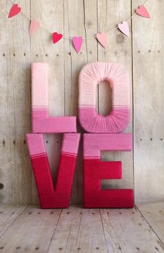 the word love is made out of pink yarn and paper hearts on a wooden background