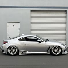 a silver sports car parked in front of a garage door with roller doors on the side