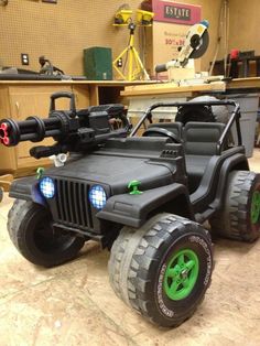 two toy jeeps with lights on in a garage area, one is black and the other is green