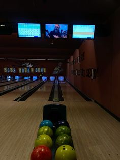 a bowling alley with several colorful bowling balls in the lanes and two televisions above