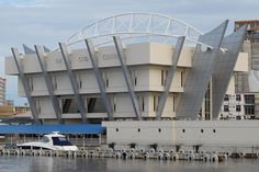 a white boat is docked in front of a large building that has a curved roof