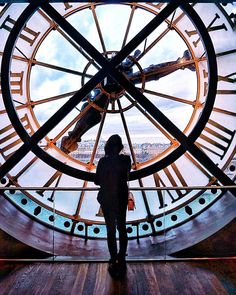 a person standing in front of a large clock with roman numerals on it