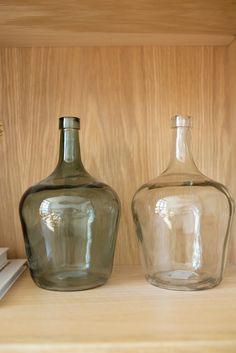 two glass vases sitting on top of a wooden shelf next to a bookshelf