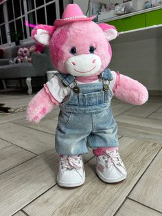 a pink teddy bear wearing overalls and a hat on the floor in a room