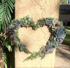 a heart shaped wreath is hanging on the side of a wall next to a palm tree