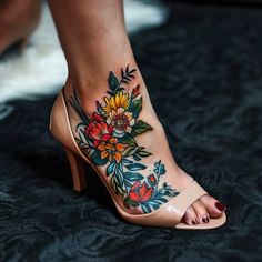 a woman's foot with tattoos on it and flowers on the side, while she is wearing high heeled sandals