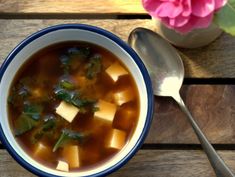 a bowl of soup with tofu and spinach in it next to a spoon