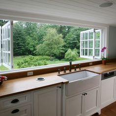 a kitchen with white cabinets and wooden counter tops next to a large window that looks out onto the yard