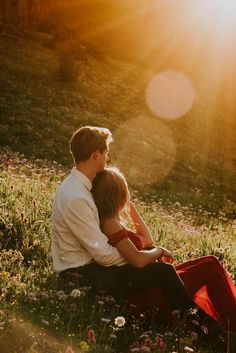 a man and woman sitting in the grass with sun shining down on their faces behind them