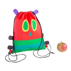 an apple sitting next to a colorful backpack with eyes and ears on the side,