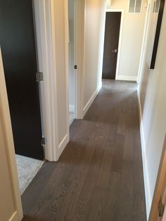 an empty hallway with wood floors and black door on one side, and white walls on the other